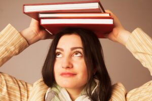 אישה מחזיקה על ראשה ערימת ספרים.